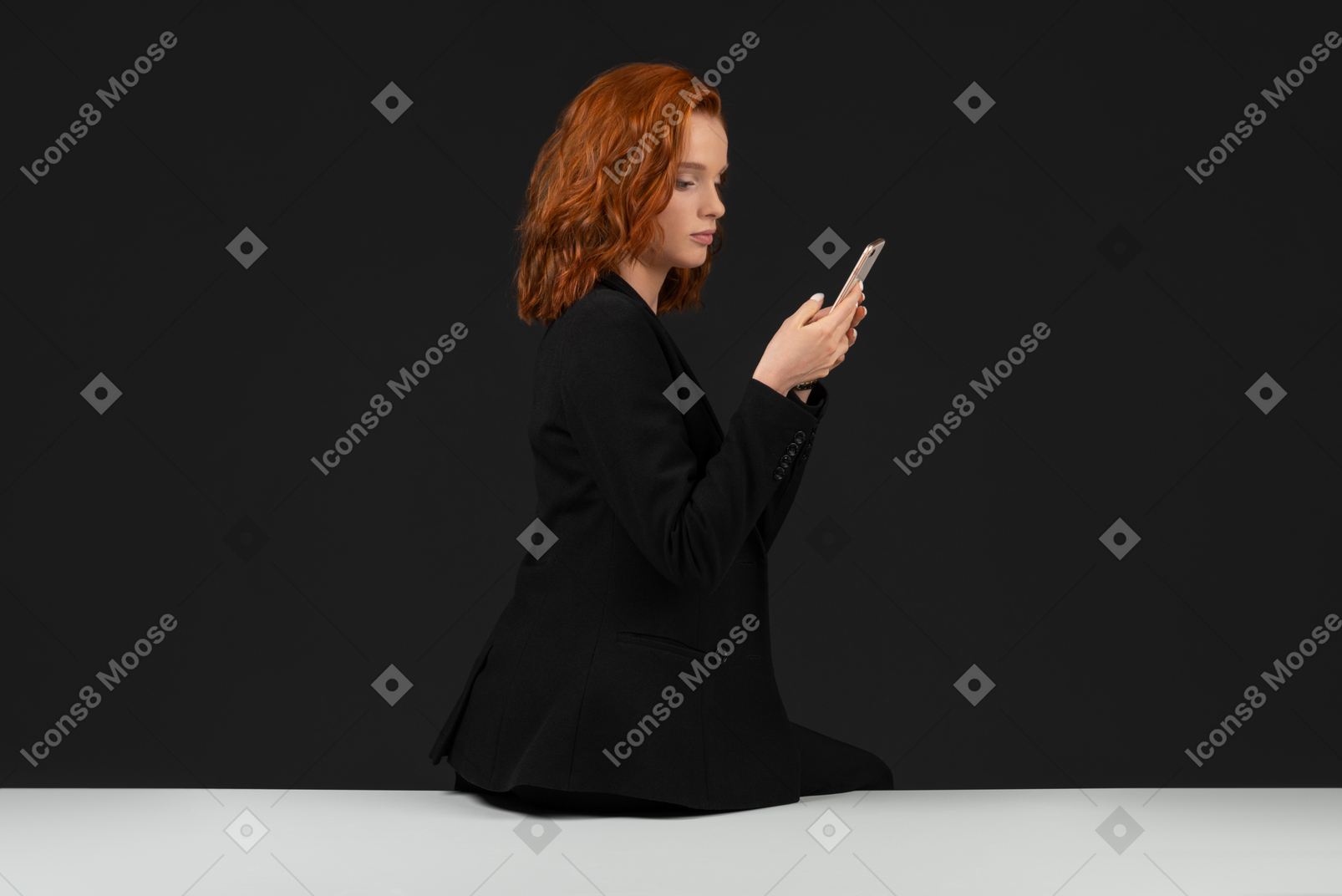 A side view of the cute girl sitting on the table and holding the phone