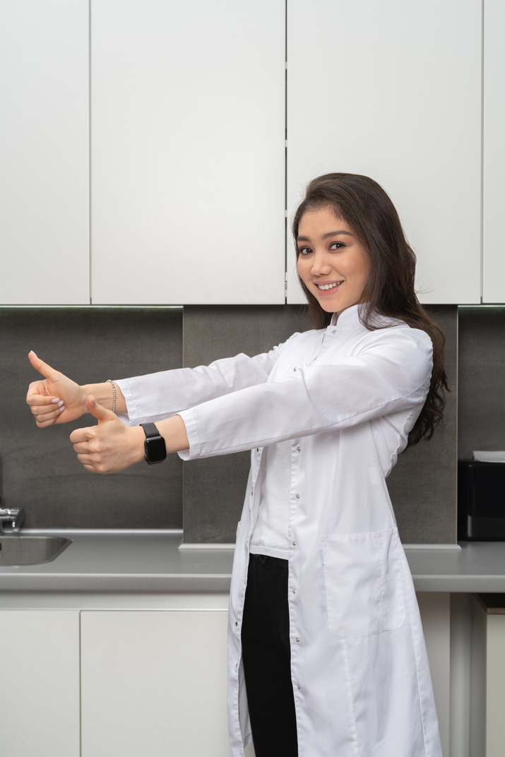 A smiling female nurse showing like gesture with both her hands looking at camera