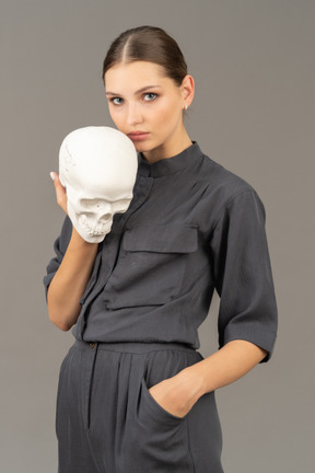 Front view of a young woman in a jumpsuit holding a plaster skull