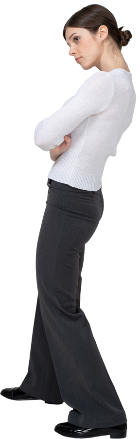 Three-quarter back view of a young woman in office clothing crossing arms