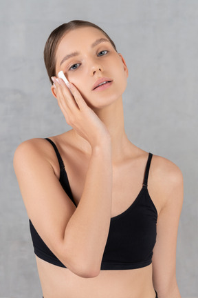 Attractive young woman removing makeup from her face with cotton pad