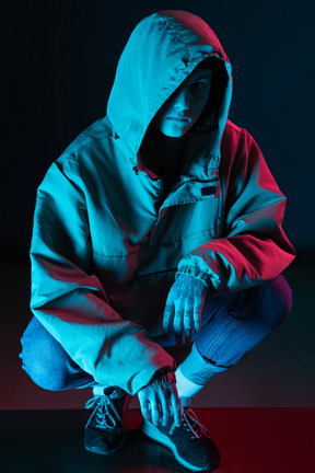 Male model in hoodie sits under blue light