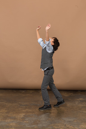 一个穿着西装的男孩举起双臂站立的侧视图