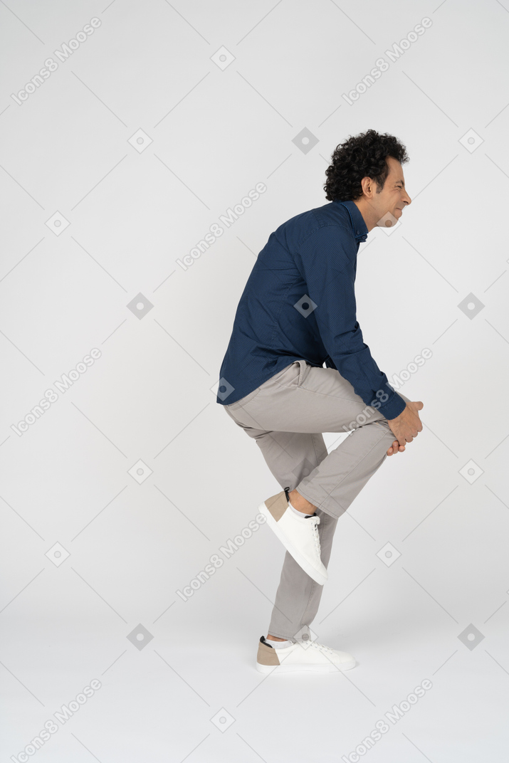 Side view of a man in casual clothes touching his hurting knee