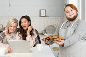 A man offering cookies to couple of women with tablet