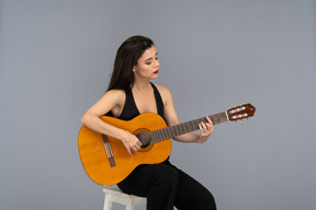 Front view of a sitting young lady in black suit playing guitar