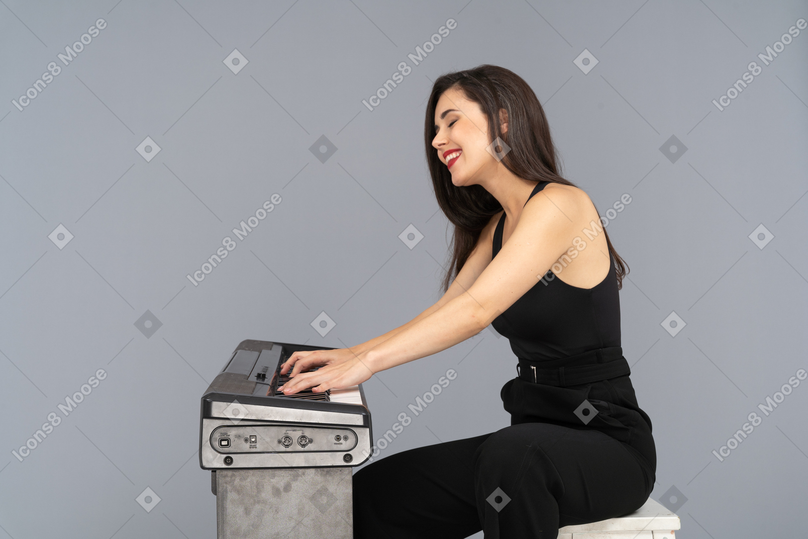 Side view of a smiling sitting young lady in black suit while playing the piano
