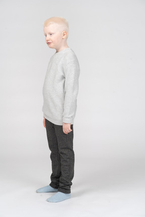 Озадаченный мальчик, стоя в сером свитере и щурясь губами