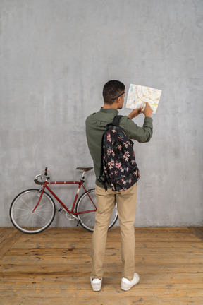 Back view of a man with a backpack examining a map
