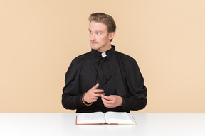 Pensive catholic priest sitting in front of open bible