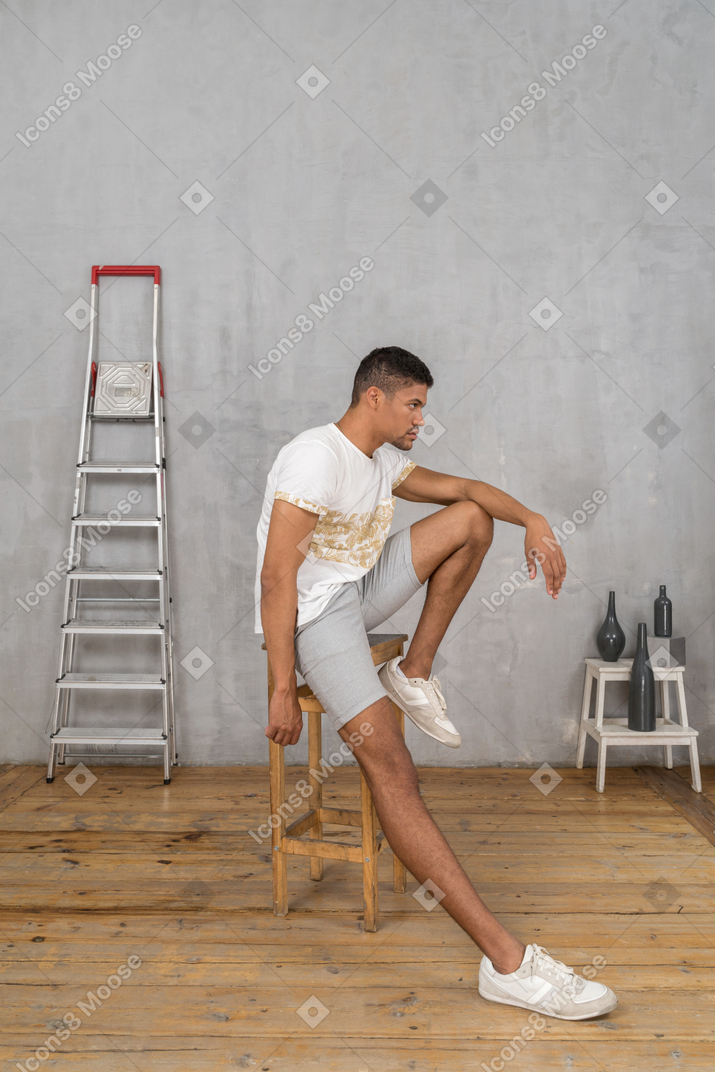 Side view of young man sitting on stool and looking forward