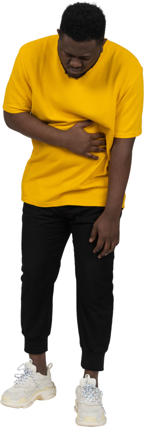 Front view of a young dark-skinned man in yellow t-shirt touching stomach