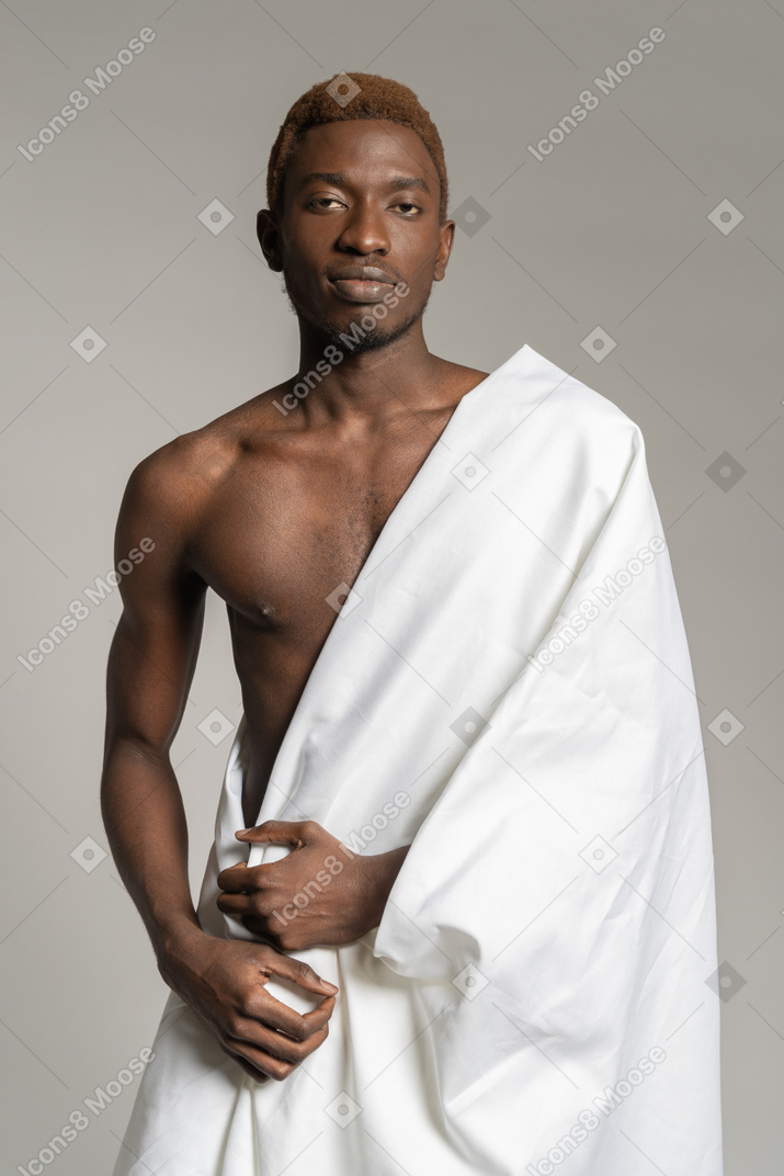 Joven negro parado en una sábana blanca y mirando a la cámara