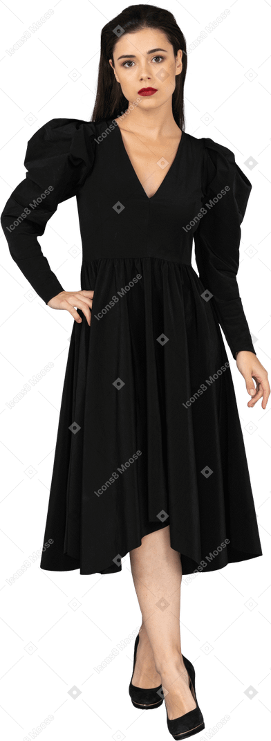 Vista frontal de una joven en un vestido negro poniendo la mano en la cadera