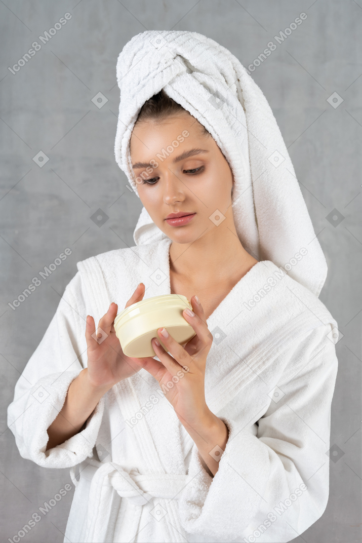 Retrato de uma mulher de roupão aplicando creme para as mãos