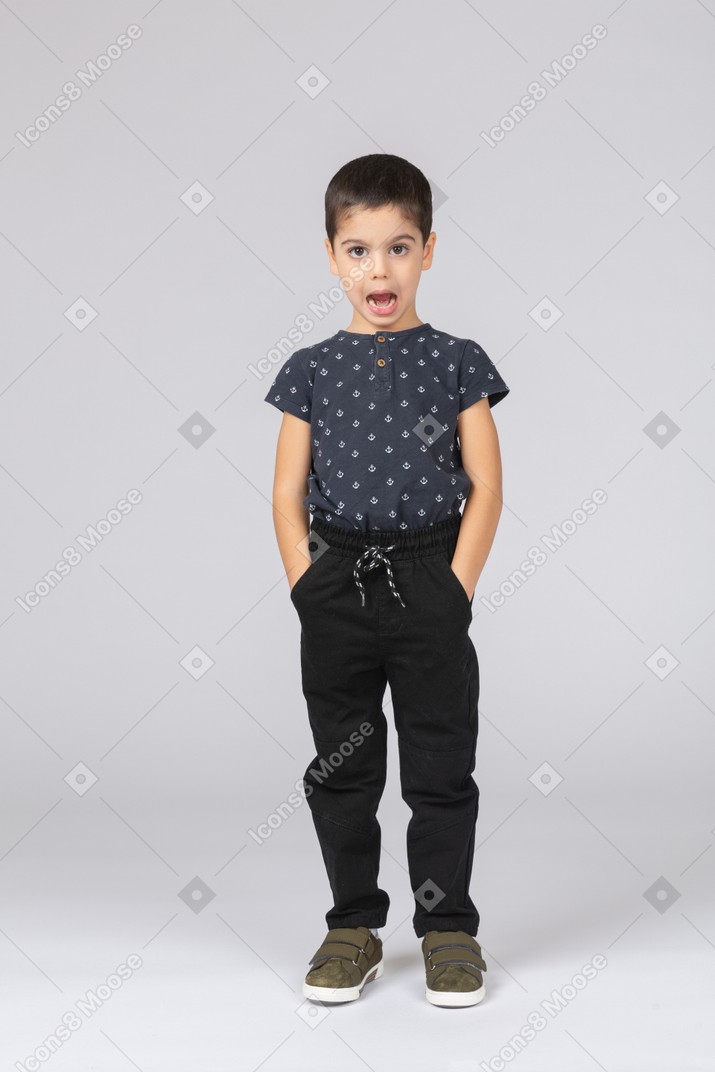 Vue de face d'un garçon mignon debout avec les mains dans les poches et regardant la caméra
