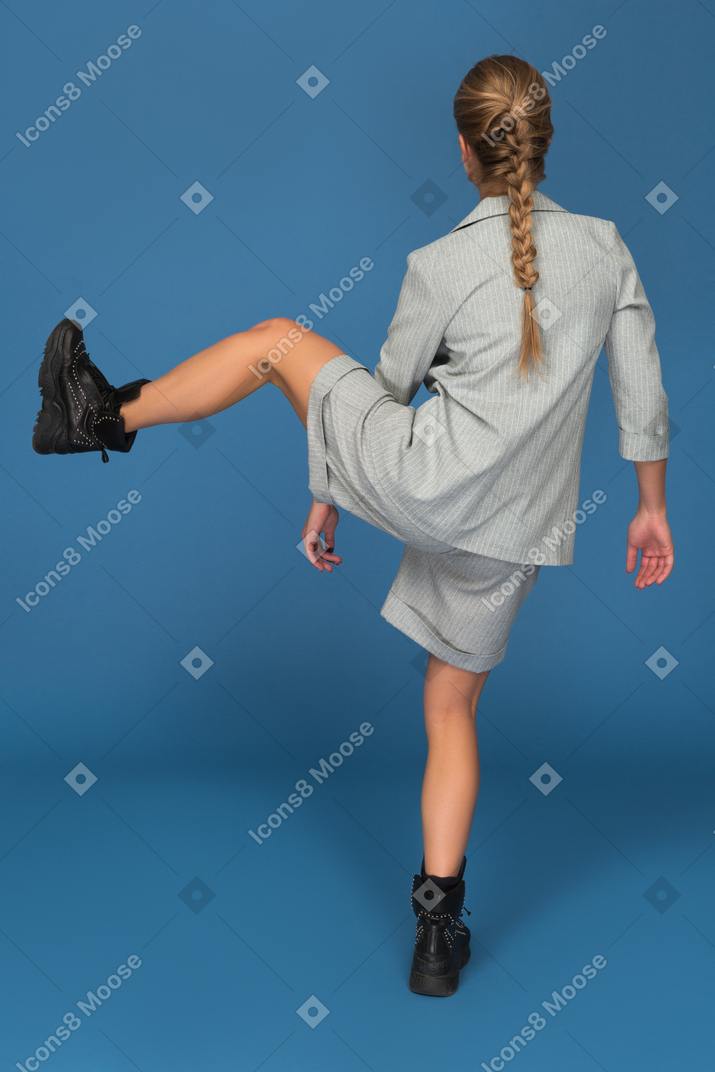 Woman lifting her one leg while standing backwards to camera