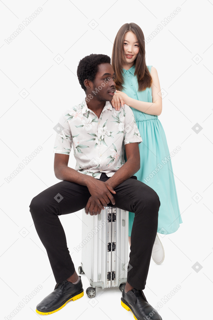 Man sitting on suitcase and woman leaning on man's shoulders