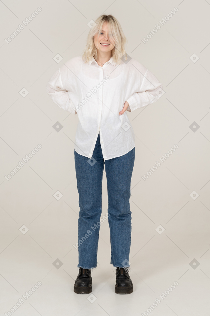 Vue de face d'une femme blonde dans des vêtements décontractés mettant les mains sur les hanches et souriant