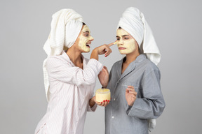 Deux, jeunes filles, cheveux, enveloppé dans, serviettes, appliquer, crème, masques, visage