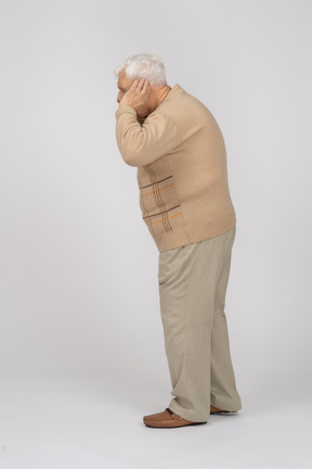 Vista lateral de un anciano con ropa informal sostiene la mano al lado de la oreja