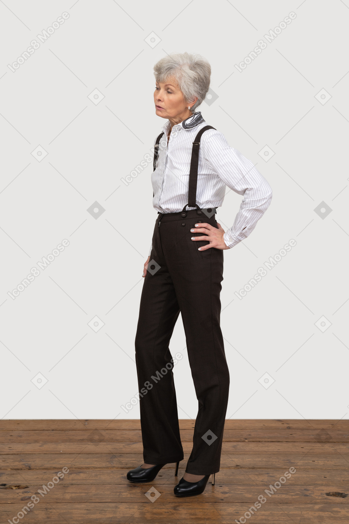 Three-quarter view of a displeased old lady in office clothing putting hands on hips