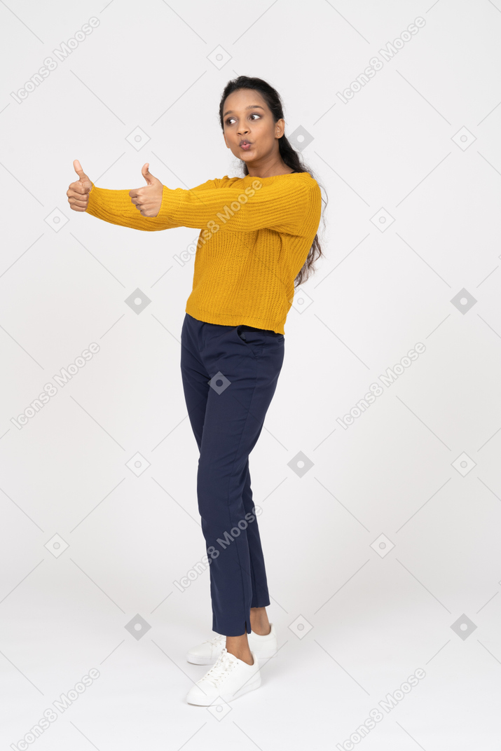 Vista lateral de uma garota com roupas casuais mostrando os polegares para cima e fazendo caretas