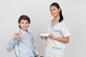 Kid boy patient holding toothbrush and female dentist holding toothpaste