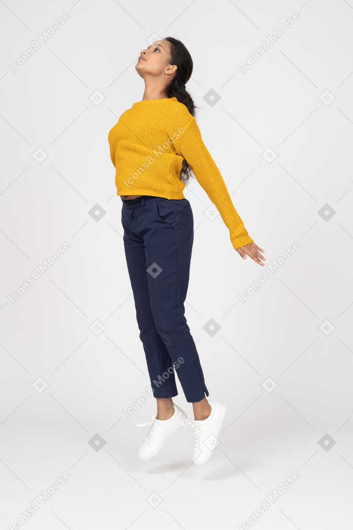 Vista lateral de uma garota com roupas casuais pulando com os braços estendidos