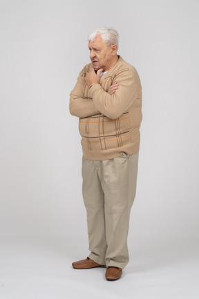 Вид спереди задумчивого старика в повседневной одежде, стоящего с рукой на подбородке