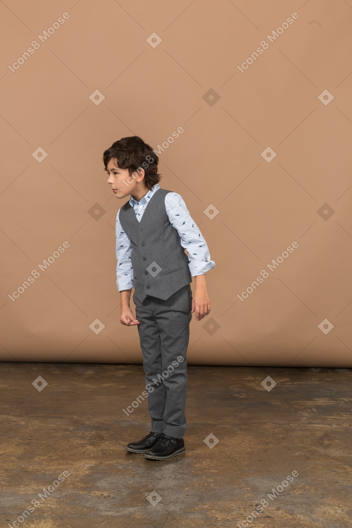 Vista frontal de un chico lindo con traje gris mirando algo con interés