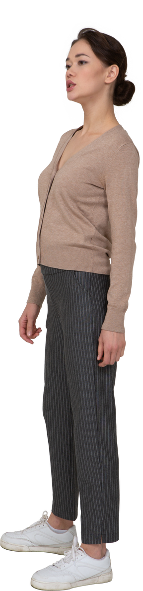 Вид в три четверти молодой леди, стоящей неподвижно в пуловере и штанах и смотрящей в сторону
