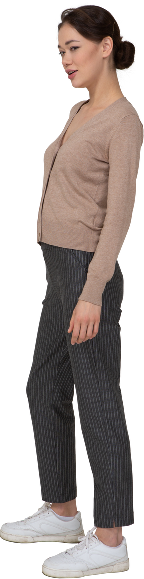 Vista de tres cuartos de una joven astuta que se queda quieta en suéter y pantalones