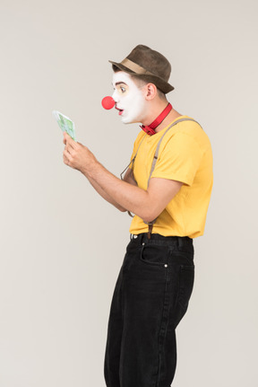 Surprised male clown standing in profile and looking at money bills he's holding