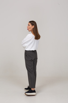 Vista posterior de tres cuartos de una joven en ropa de oficina mostrando la lengua