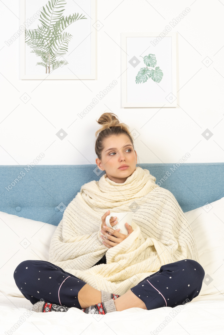 一个生病的年轻女士裹着白色毯子住在床上的前视图