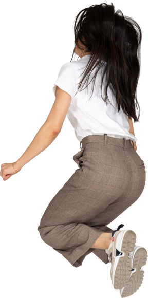 Vista posteriore di tre quarti di una giovane donna che salta in calzoni e t-shirt piegando le ginocchia