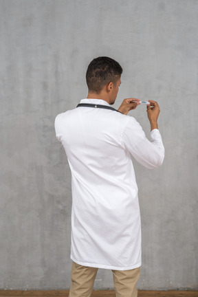 Back view of a male doctor holding a thermometer