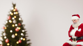 A man dressed as santa claus sitting in front of a christmas tree