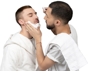 Young caucasian man carefully shaving his partner and touching his cheek