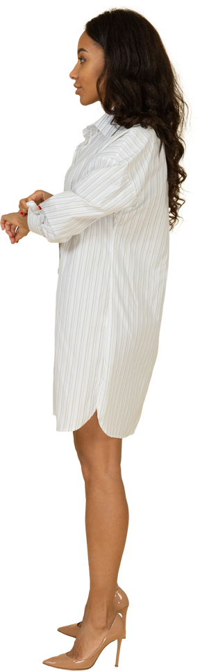 Vista lateral de una mujer joven de piel oscura con vestido blanco abotonándose la manga