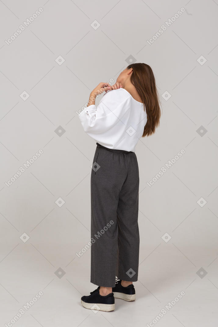 Vista posterior de tres cuartos de una joven en ropa de oficina ajustando su blusa