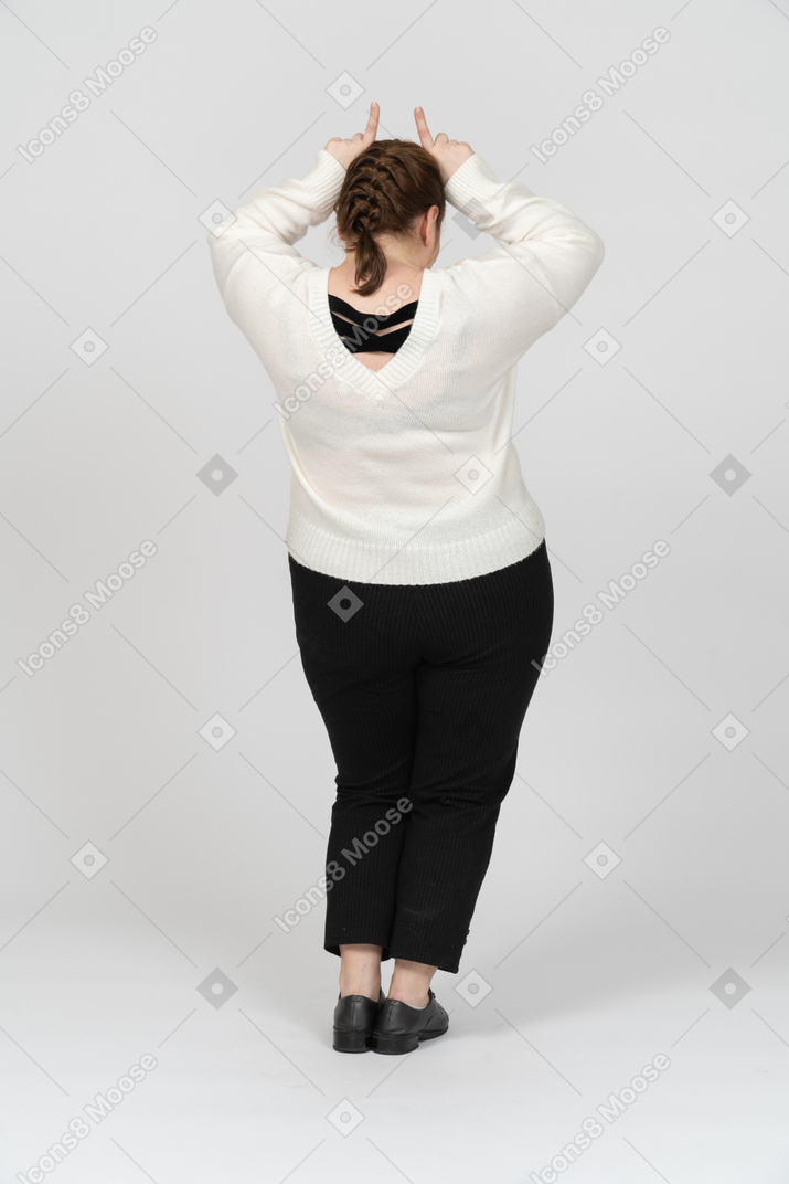 Вид сзади пухлой женщины в повседневной одежде, делающей рога