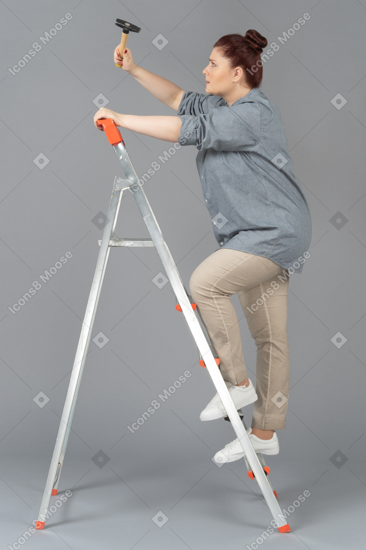 Young woman standing sideways on stepladder and hammering