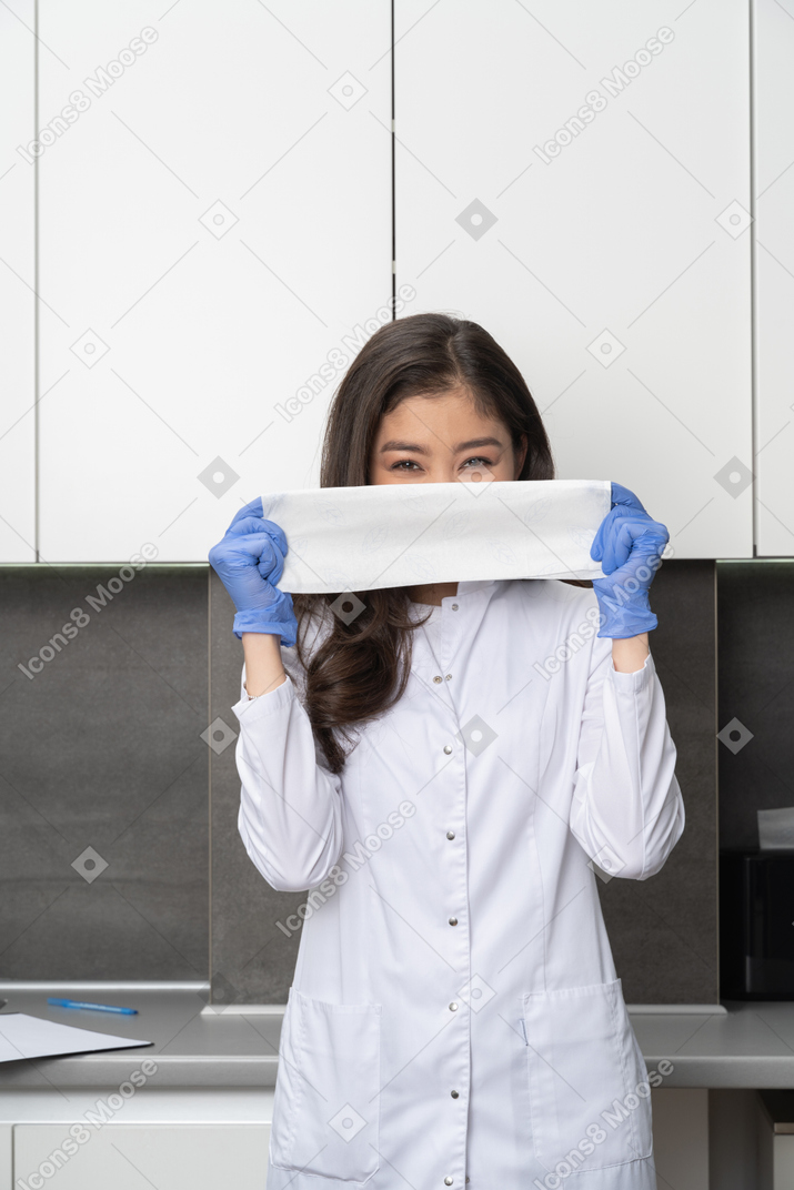 Front view of a young female doctor holding a cloth in protective gloves and narrowing eyes
