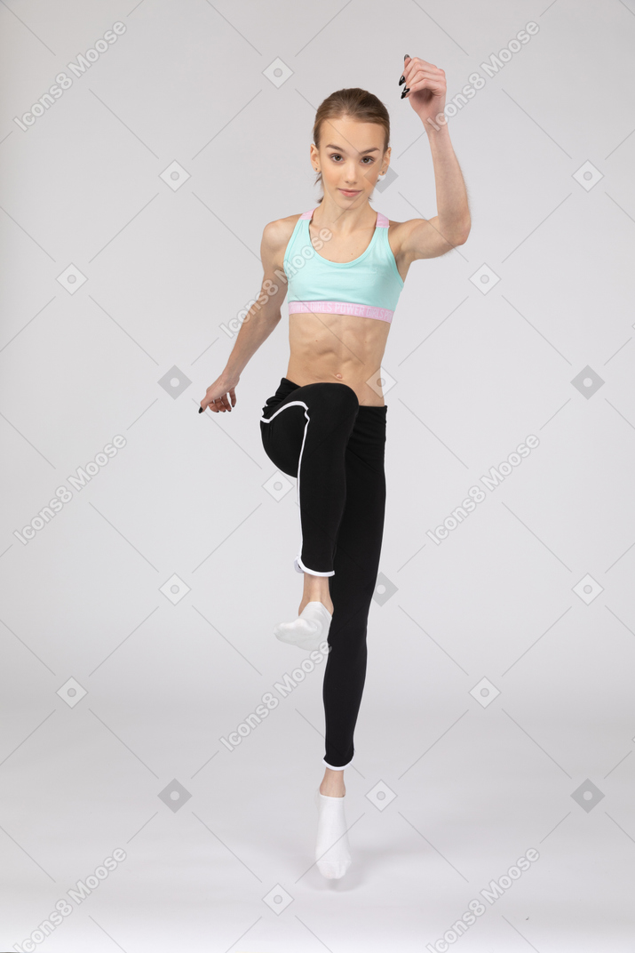 Front view of a teen girl in sportswear raising hand and leg
