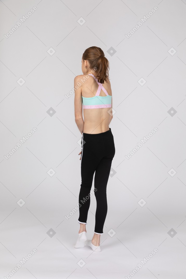 Back view of a shy teen girl in sportswear holding hands together