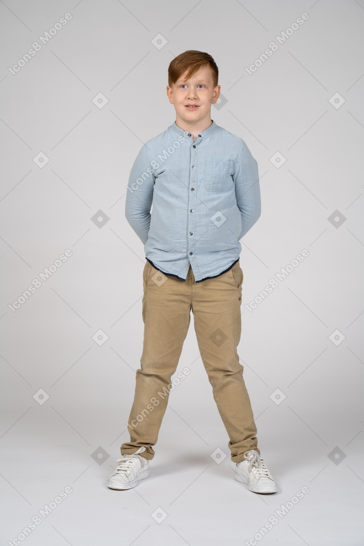 Front view of a cute boy standing with hands behind back