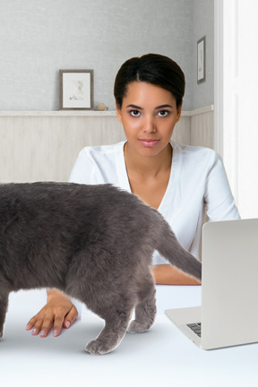 A cat walking on a desk in front of a woman with laptop