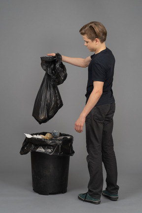 Um jovem segurando um saco de lixo acima de uma lixeira